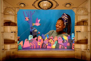 Multicoloured cardboard bird puppets with woman singing in cardboard theatre