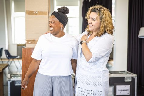 Two women in white shirts stand smiling with their arms around each other's waists