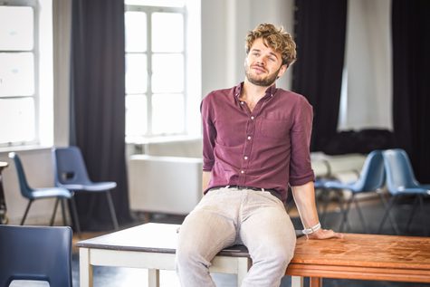 A man in a maroon shirt sits on a table.