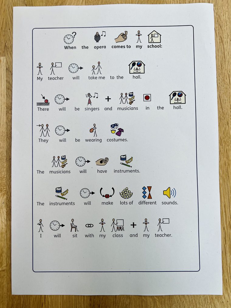 One sheet of white paper sits on a wooden table. A social story explaining what happens during an opera performance at a school is on the page.