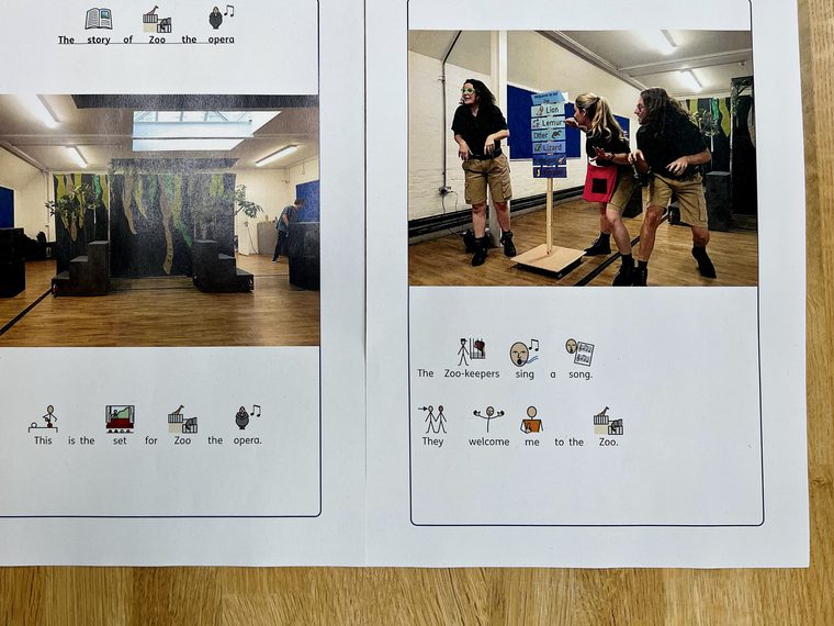 Two white sheets of paper sit side by side on a wood table. Printed on the papers are pictures and social stories explaining the plot of Zoo! the opera.