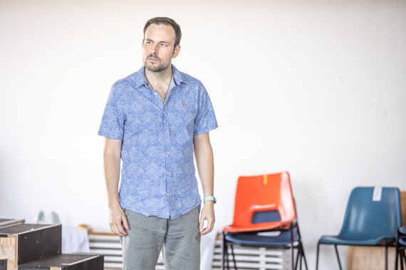 A man in a blue shirt stands in the rehearsal room