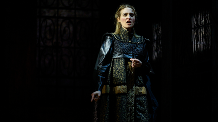 Lucrezia Borgia stands wearing battle clothing centre stage. She is singing angrily.