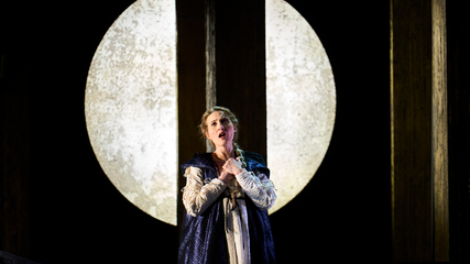 A female wearing period clothing stands against a moon backdrop, with her hands clasped