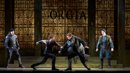 Four men in period clothing are onstage, in front of large metal gates. Two men are fighting.