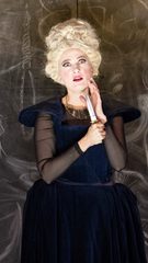 A woman with a tall beehive wig and dressed in blue holds a dagger to her hand