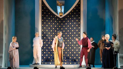 Eight people in period costume stand in a line on stage