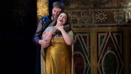 A bearded man embraces a woman in a gold dress, both laughing with happiness