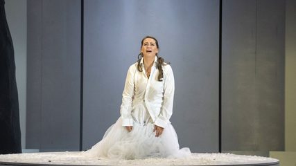 A woman in white shirt and white skirt kneels on a rostrum
