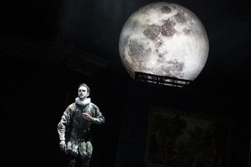 There is a large moon in the background. Aeneas is in the forefront wearing a Tudor outfit and wearing a ruff