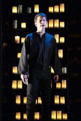 The Sailor is standing in all black with shelves of lanterns behind him