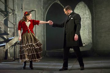 Don Giovanni and Zerlina are holding hands. They are both smiling and Don Giovanni is leading Zerlina