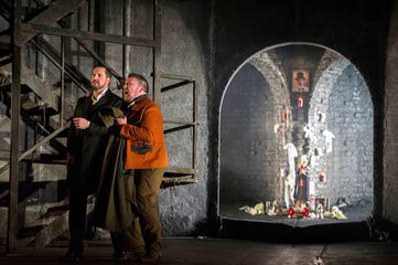 Don Giovanni and Leporello are standing stage right next to a staircase. Leporello is holding his coat and Don Giovanni.