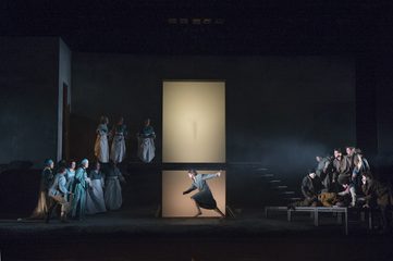 Oreste in central stage, pointing down into a hole. He is surrounded by an onlooking chorus