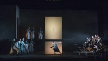 Oreste in central stage, pointing down into a hole. He is surrounded by an onlooking chorus