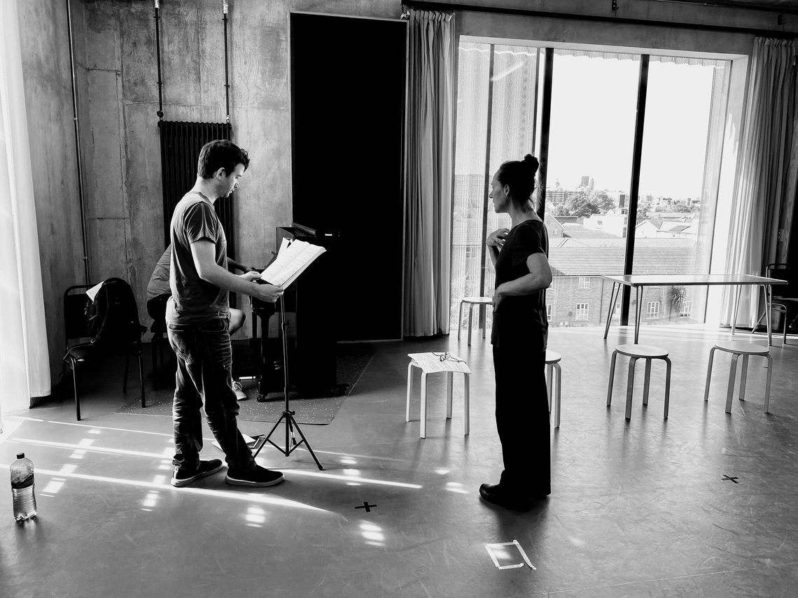 Singer looking at sheet music whilst watched by a director