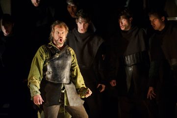 Nello singing in front of chorus of men