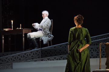 Scarpia sealing a letter as Tosca conceals a dagger behind her back