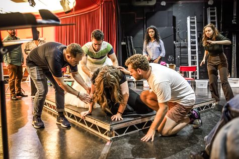 A woman crouches on the floor with three men bent down around her.